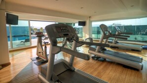 A gym with treadmills and exercise equipment, large windows, and a pool visible through the glass. - Presidente InterContinental Guadalajara by IHG (Zapopan)