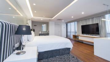 Una habitación de hotel moderna con una cama grande, un televisor de pantalla plana, una mesita de noche con lámpara y un espejo amplio.