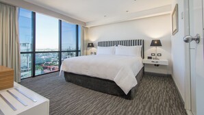 A hotel room with a large bed, two bedside tables with lamps, a view of the city through large windows, and a carpeted floor. - Presidente InterContinental Guadalajara by IHG (Zapopan)