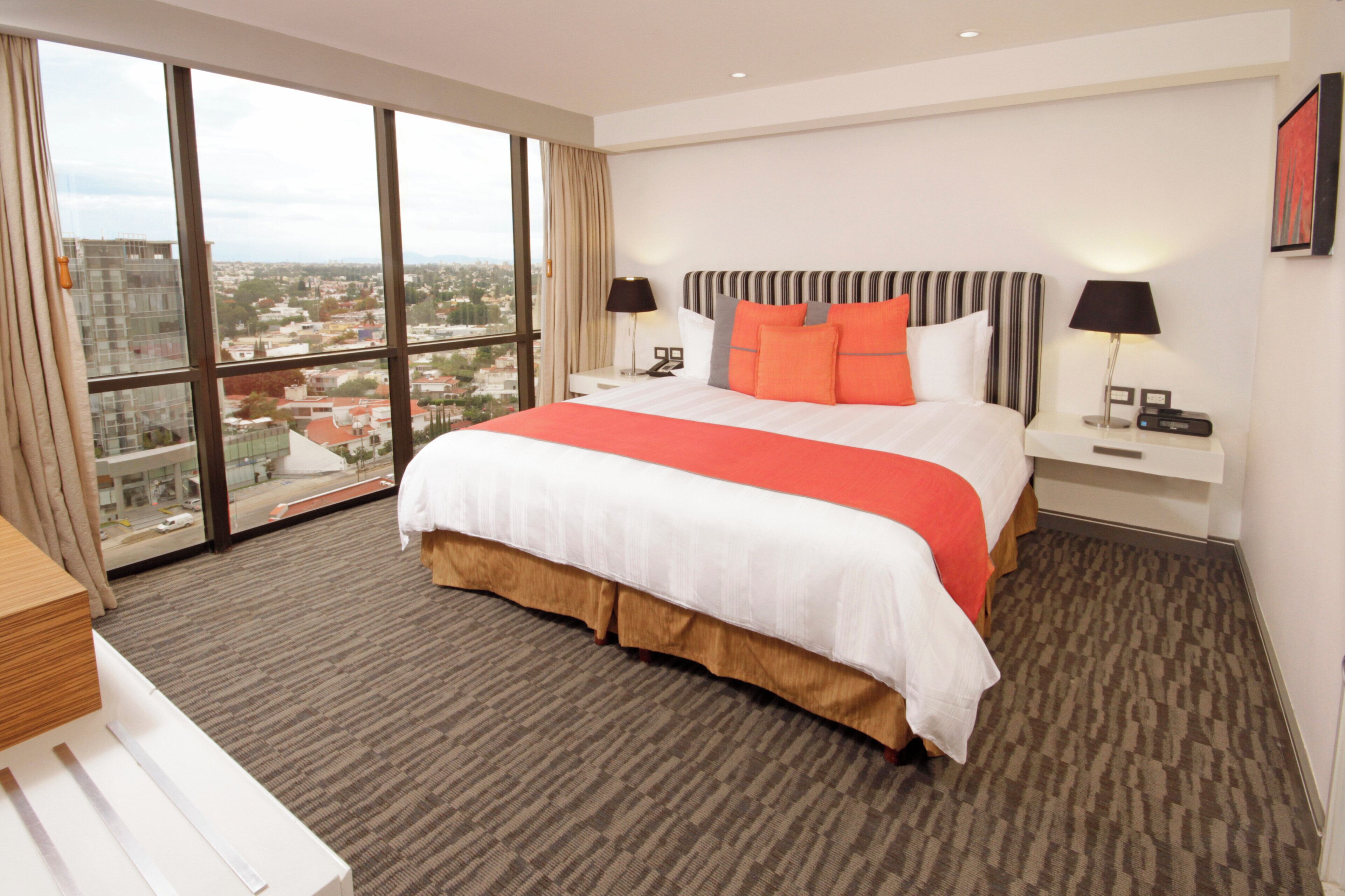 A hotel room with a large bed, two bedside tables, a view of the city, and a cityscape visible through the window.