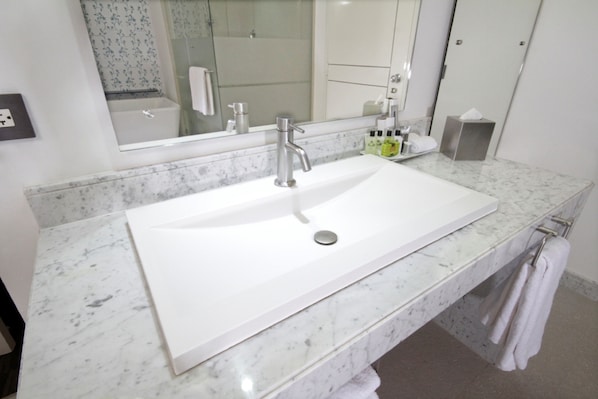 Casa de banho com lavatório branco, espelho grande e bancada de mármore.