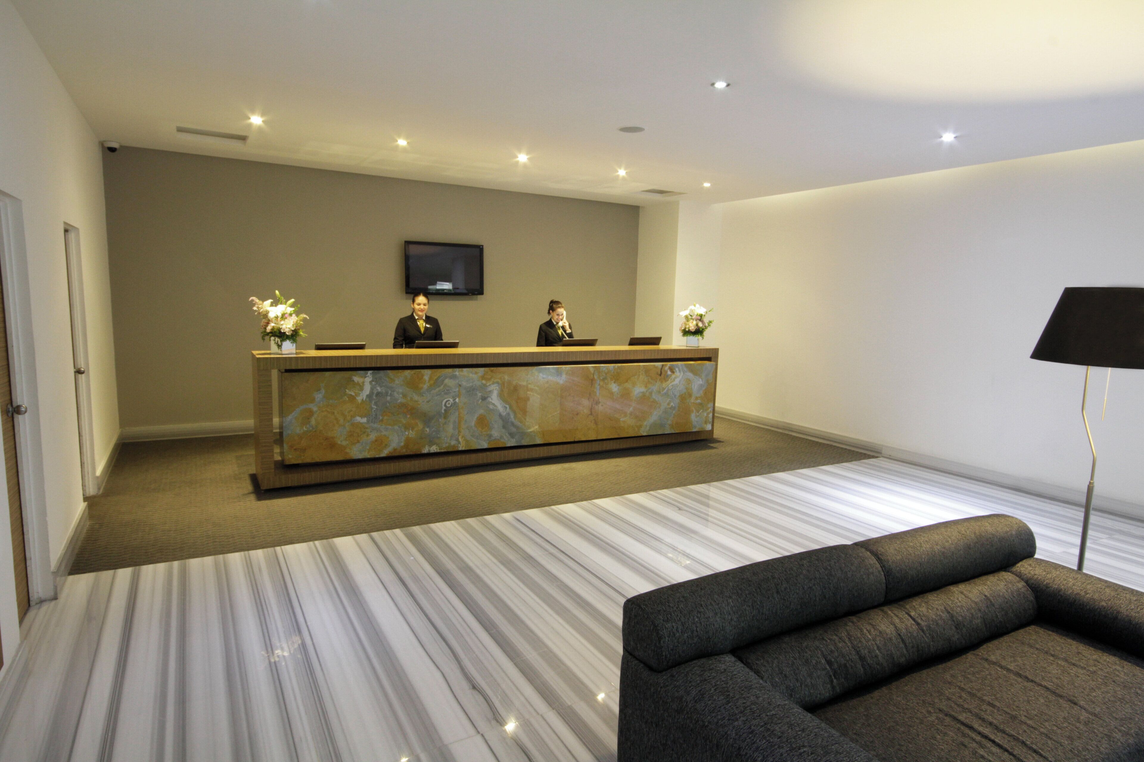 Un área de recepción con piso de mármol, una mesa de recepción, un televisor de pantalla plana y un sofá.