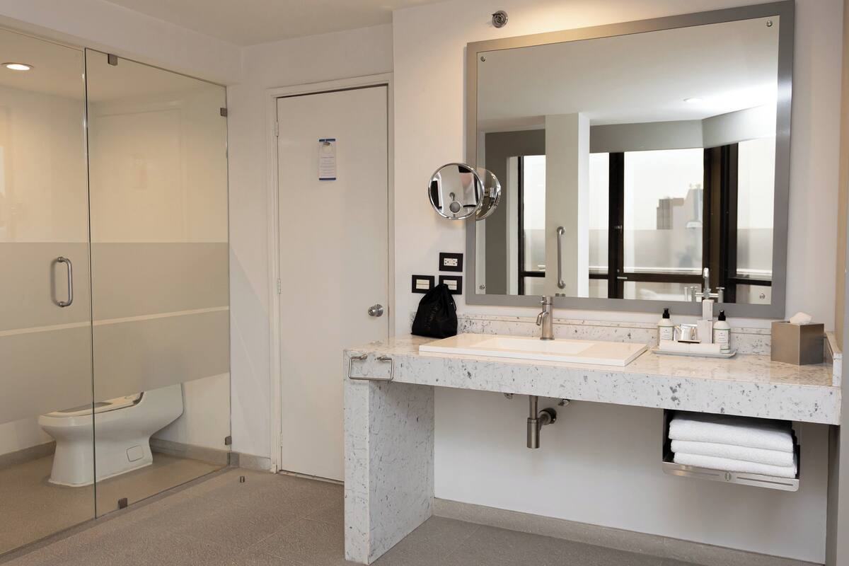 Ein modernes Badezimmer mit Duschkabine aus Glas, einer weißen Toilette, einem мрамор-Waschbecken und einem großen Spiegel.