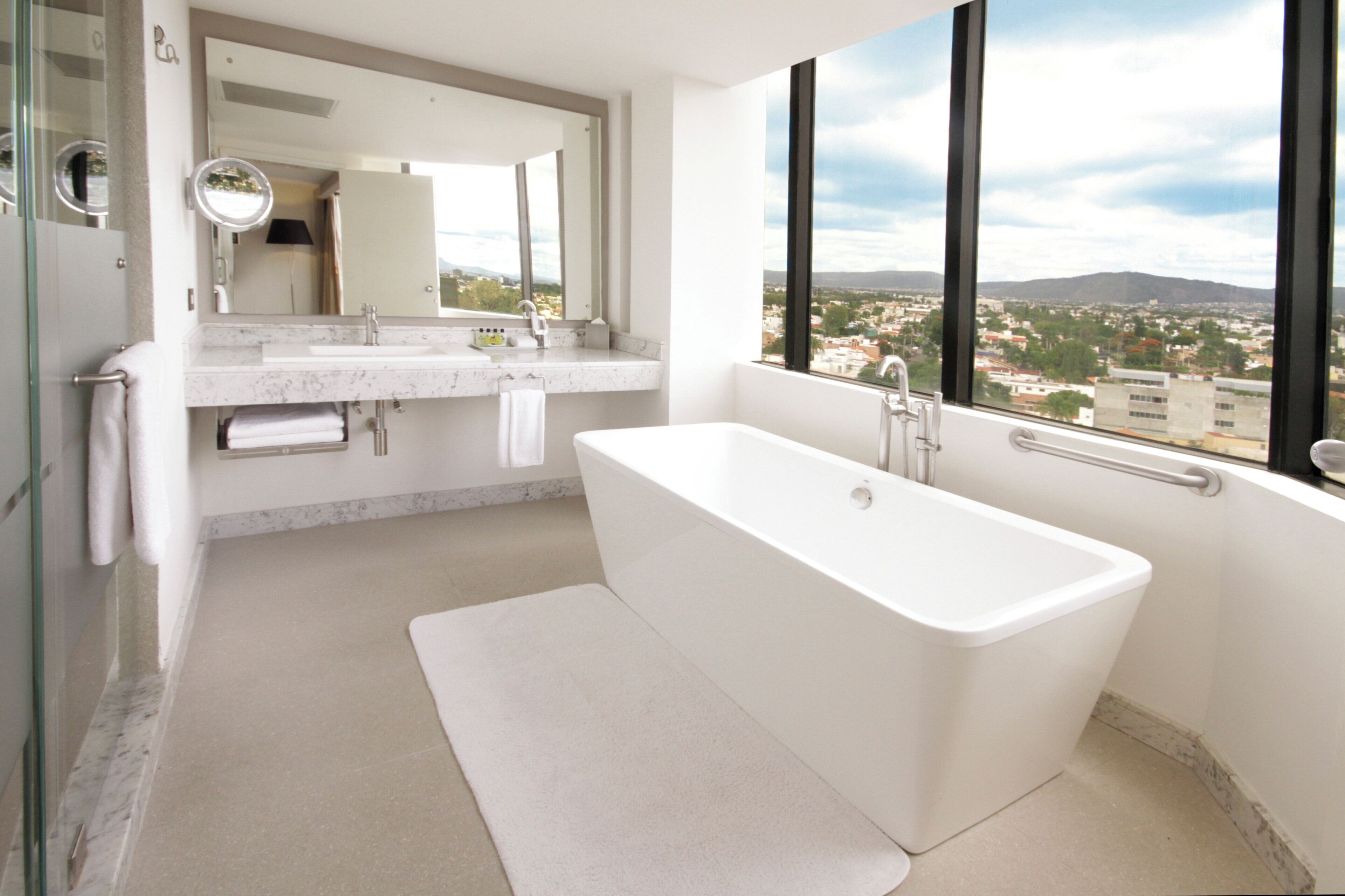 A modern bathroom with a large bathtub, a glass shower enclosure, and a view of a cityscape through large windows.