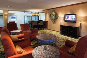 Eine Hotellobby mit roten Polsofas, einem runden Couchtisch, einem an der Wand befestigten Fernseher und einem gemusterten Teppich.