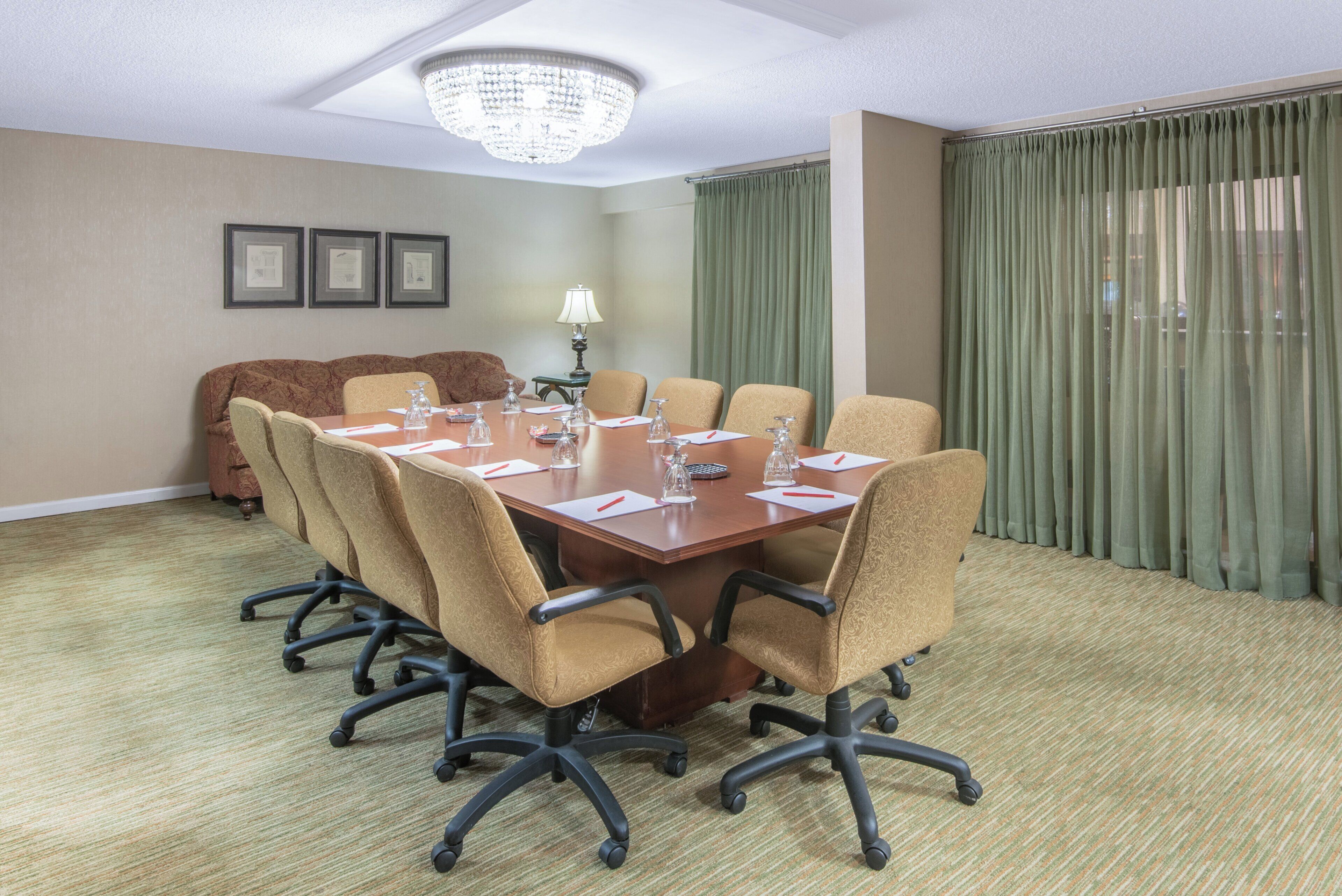 A conference room with a wooden table, six chairs, a chandelier, and a green curtain.