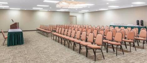 A conference room with rows of chairs, a podium, and a table with coffee and water dispensers.