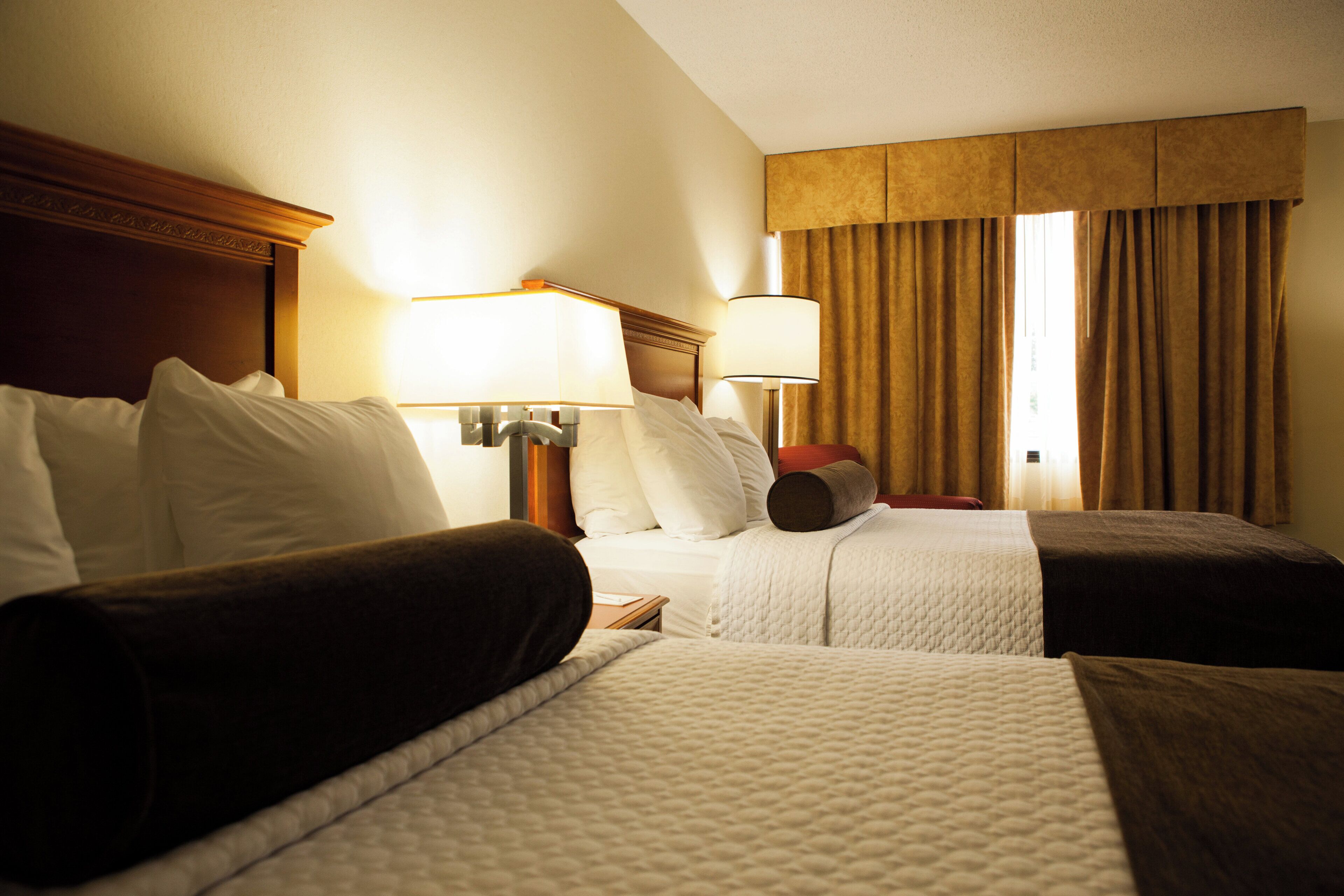 Habitación de hotel con dos camas, una mesita de noche con lámparas y una ventana con cortinas.