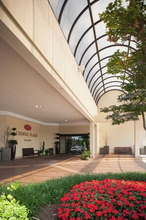 A building entrance with a glass ceiling, a sign reading 'CROWNE PLAZA HICKORY', and a landscaped area with red flowers. - Crowne Plaza Hotel Hickory by IHG (Hickory)