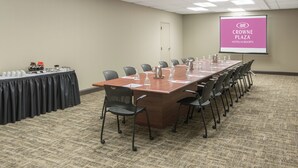 A conference room with a long table, chairs, a projector screen, and a coffee station. - Crowne Plaza Hotel Hickory by IHG (Hickory)