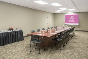 A conference room with a long table, chairs, a projector screen, and a coffee station. - Crowne Plaza Hotel Hickory by IHG (Hickory)