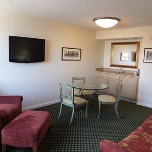 A compact living space with a flat-screen TV, a dining table with chairs, a kitchenette, and a sofa. - Crowne Plaza Hotel Hickory by IHG (Hickory)