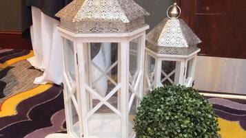 Two white lanterns with intricate metal tops, a green spherical plant, and several white candles on a patterned carpet.