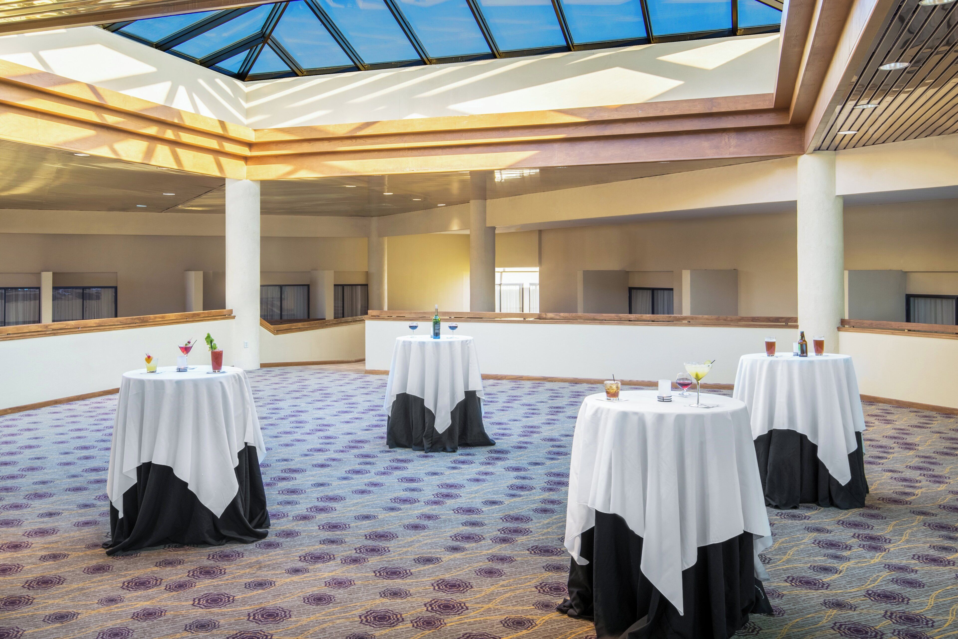 A conference room with multiple tables, each with a white tablecloth and black chair covers, and a patterned carpet.
