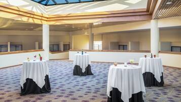A conference room with multiple tables, each with a white tablecloth and black chair covers, and a patterned carpet.