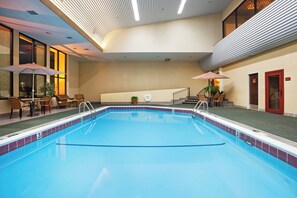 Una piscina interior con borde de azulejos, un área de descanso con sillas y mesas, y un cuarto de sauna.