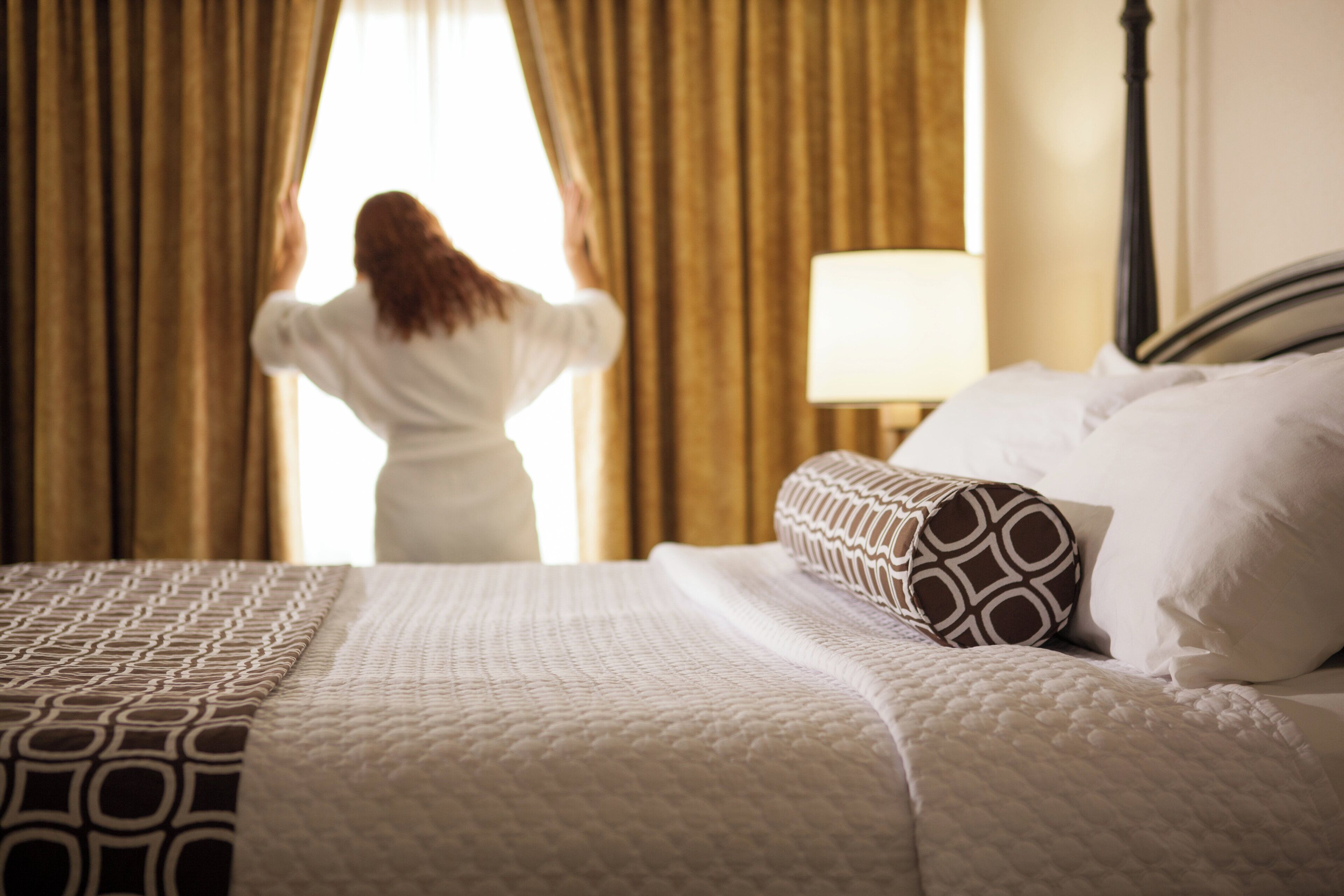 Una habitación de hotel con una cama, una lámpara y cortinas.