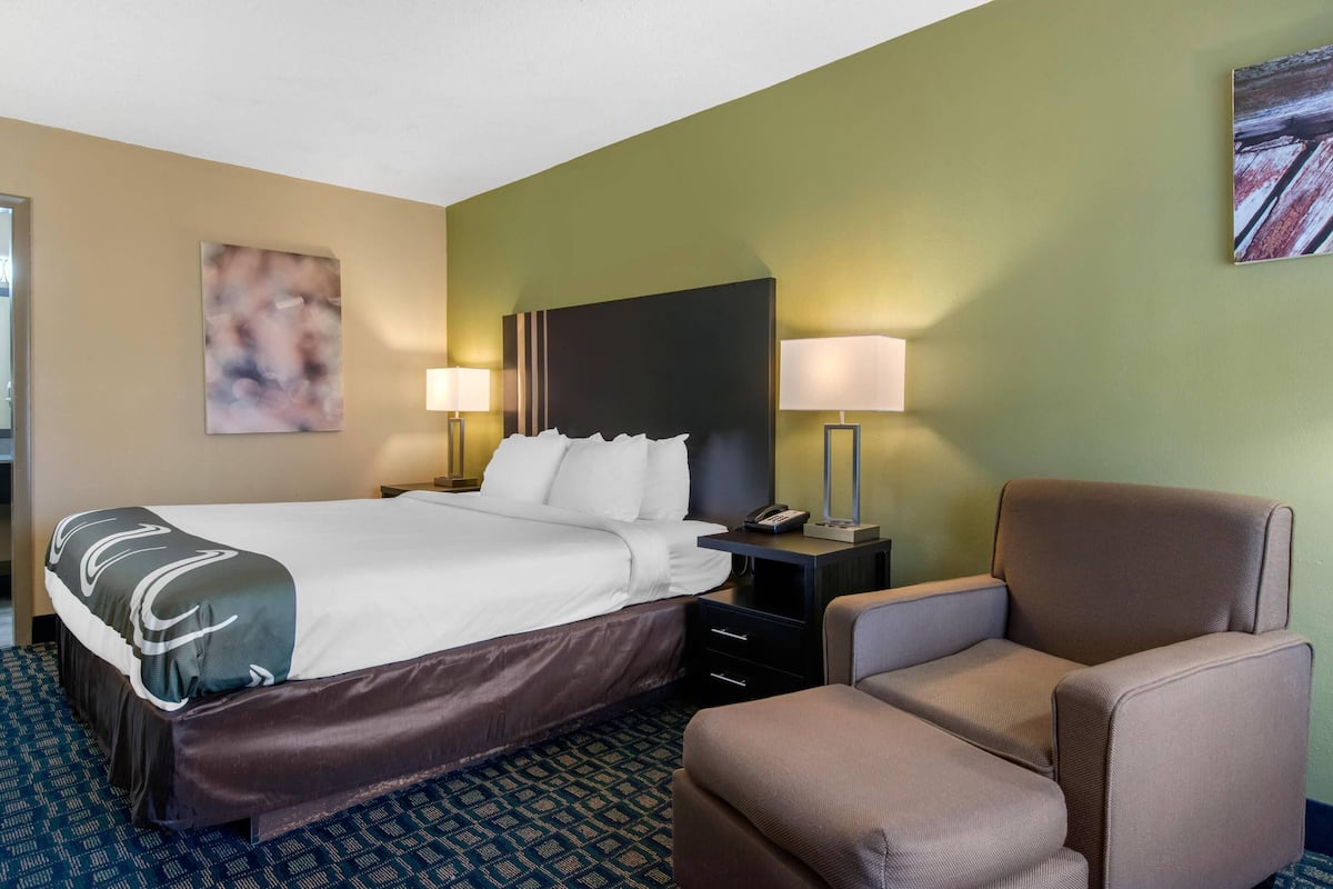 A hotel room with a bed, two bedside lamps, a chair, and a painting on the wall.