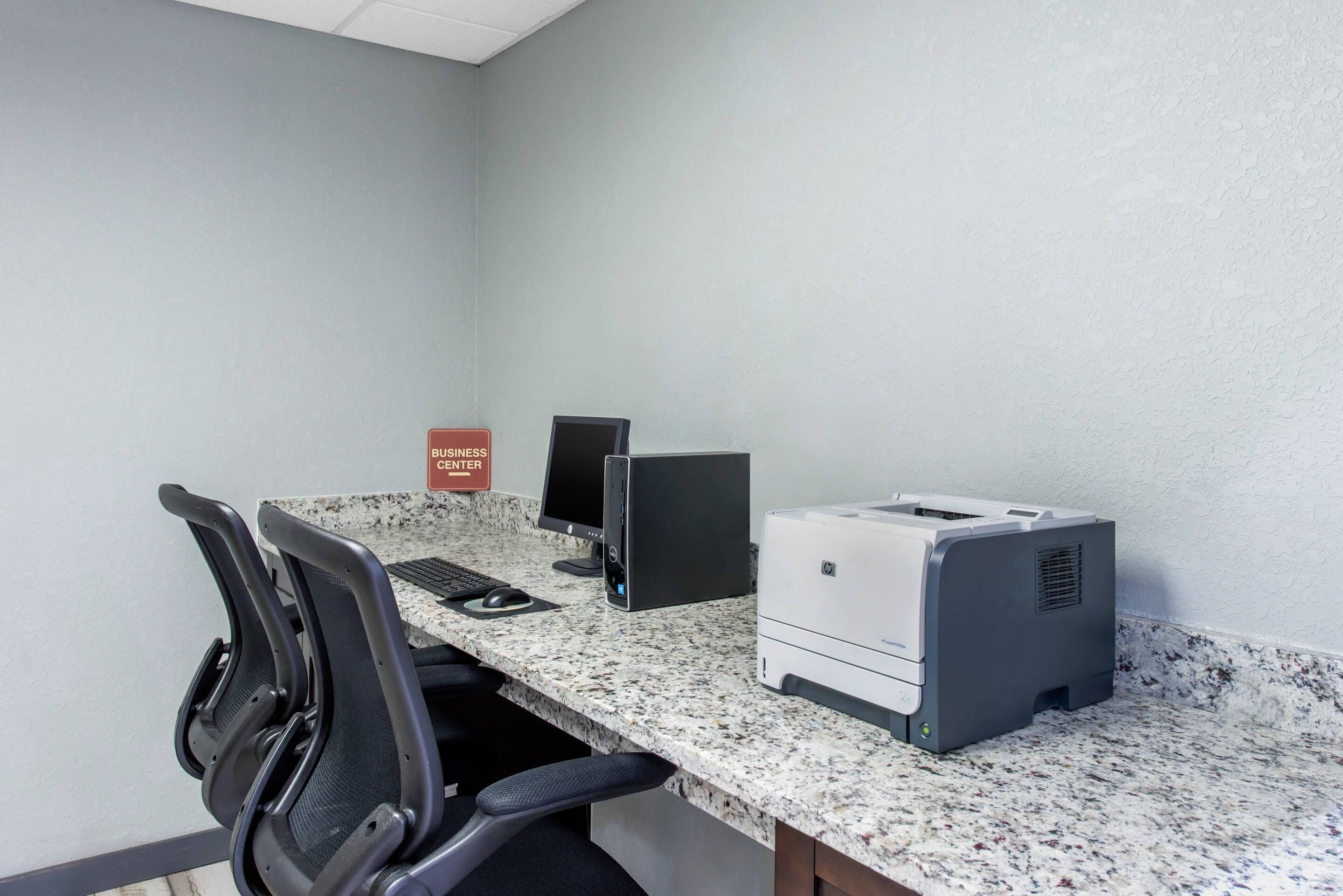 Ein Konferenzraum mit einer Granit-Arbeitsplatte, zwei Desktop-Computern, einem Drucker und vier schwarzen Bürostühlen.