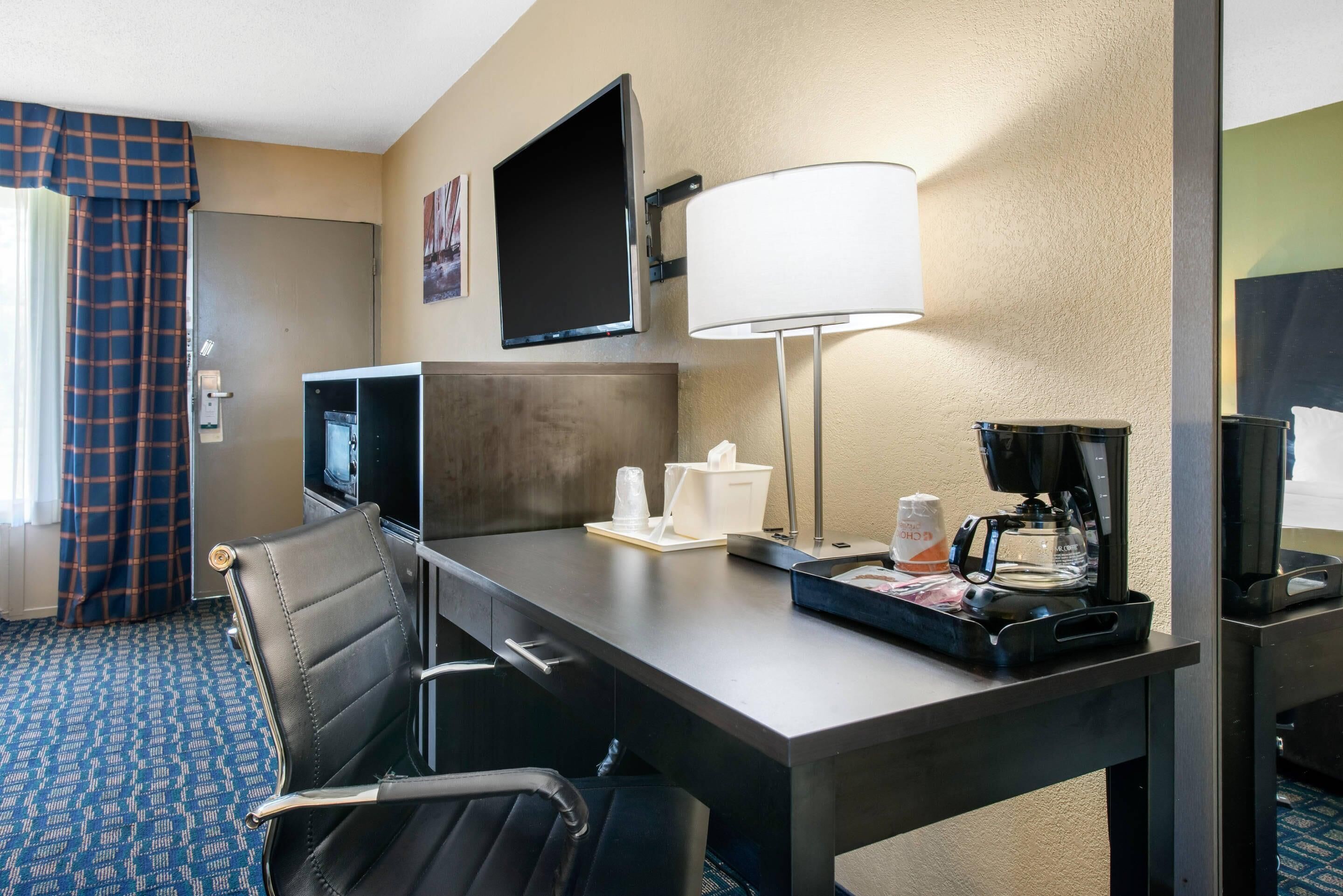 A hotel room with a desk, a television, a coffee maker, a lamp, and a chair.