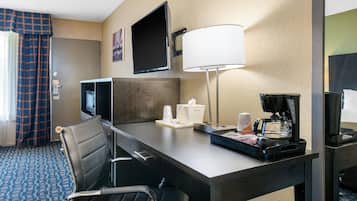 A hotel room with a desk, a television, a coffee maker, a lamp, and a chair.
