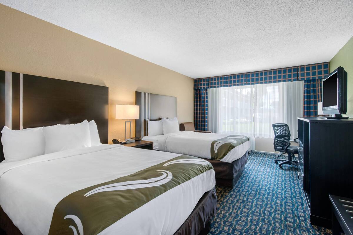 A hotel room with two beds, a desk with a computer, a TV, and a chair.