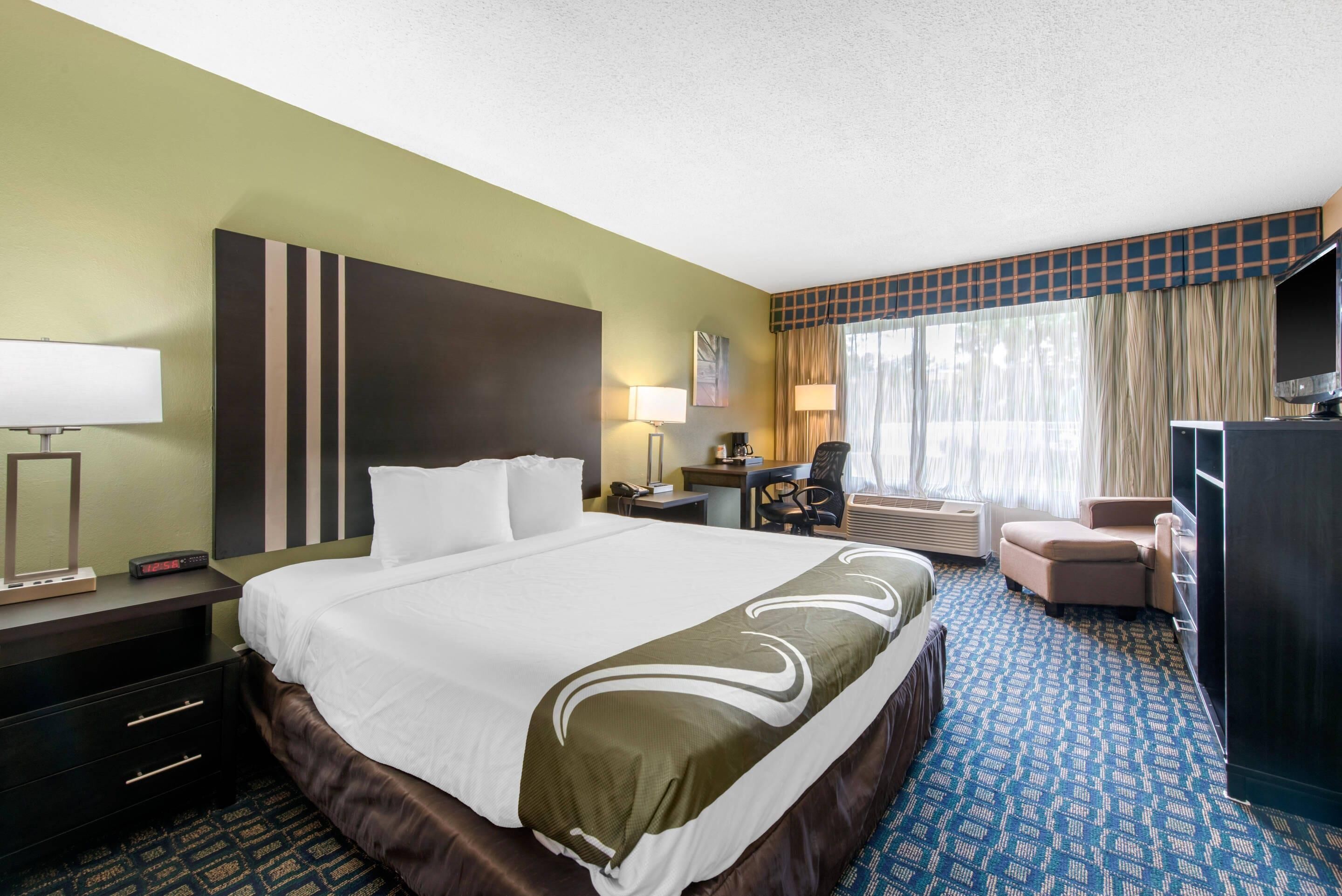 Una habitación de hotel con una cama grande, un escritorio con una silla, un televisor y una ventana con cortinas.