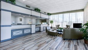 A hotel lobby with a reception desk, seating area, and a kitchen.