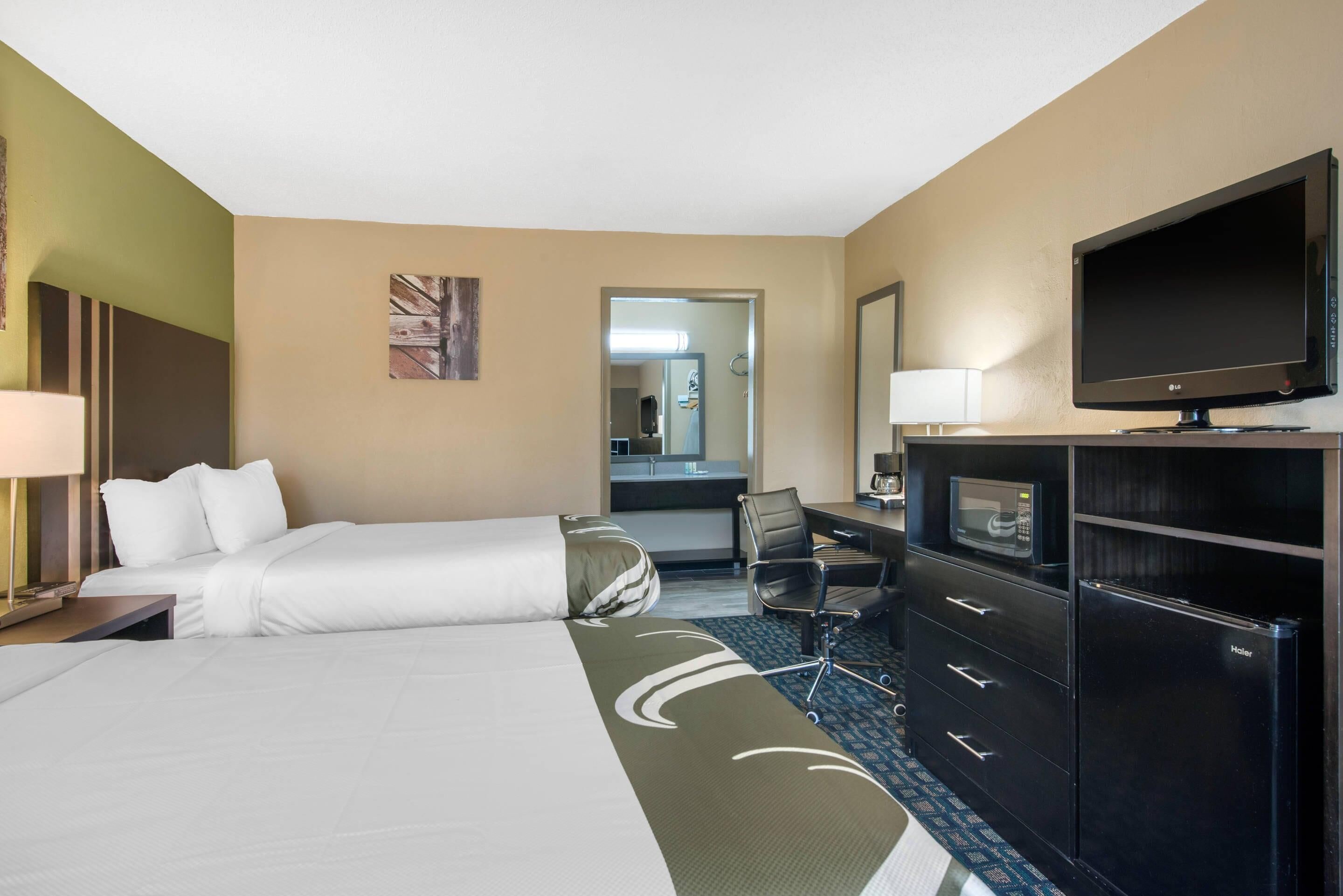 A hotel room with two beds, a desk, a chair, a television, a microwave, and a refrigerator.