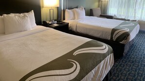 A hotel room with two beds, a nightstand with a lamp, a telephone, and a framed picture on the wall.