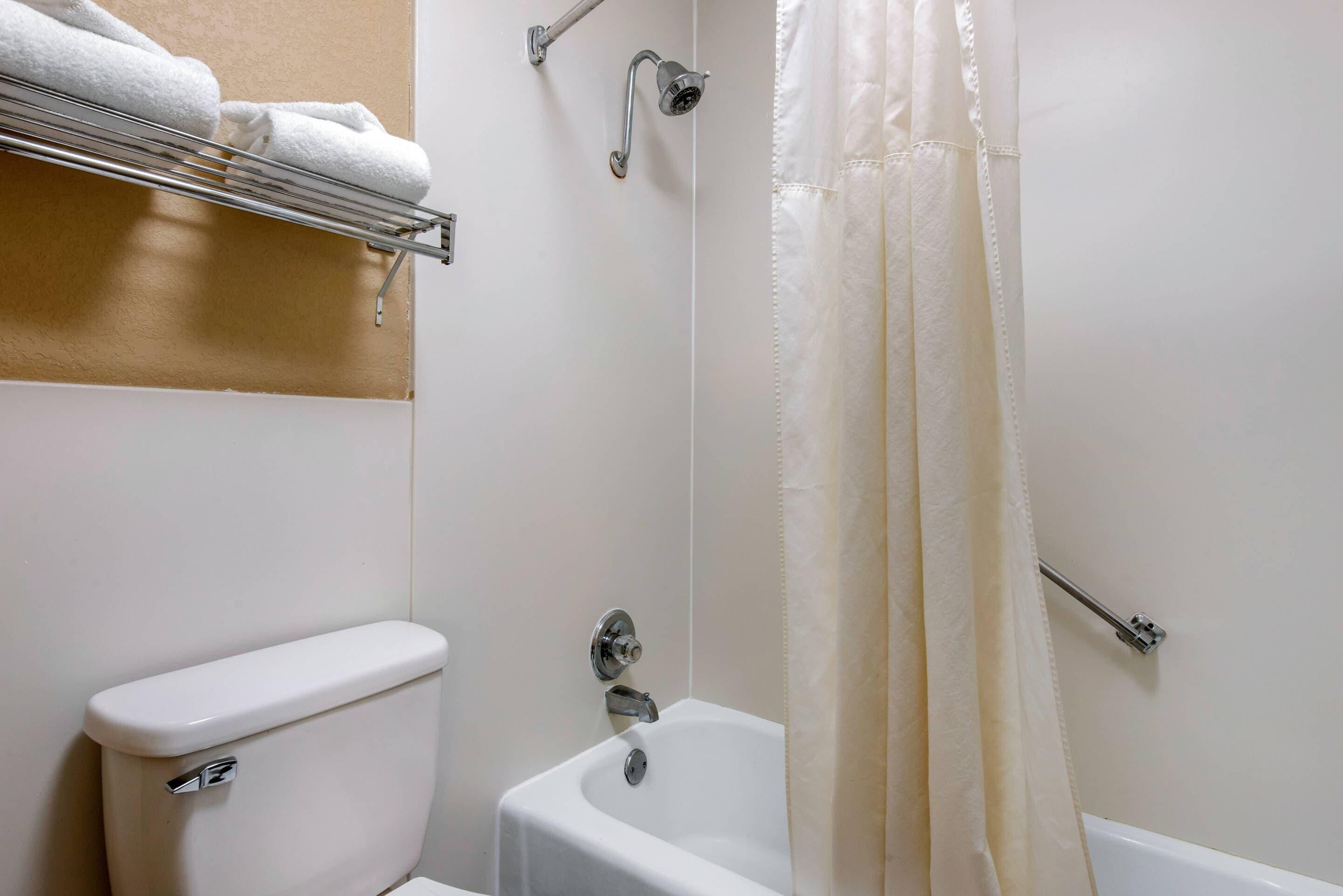 A bathroom with a toilet, a bathtub, a shower, and a towel rack with towels.