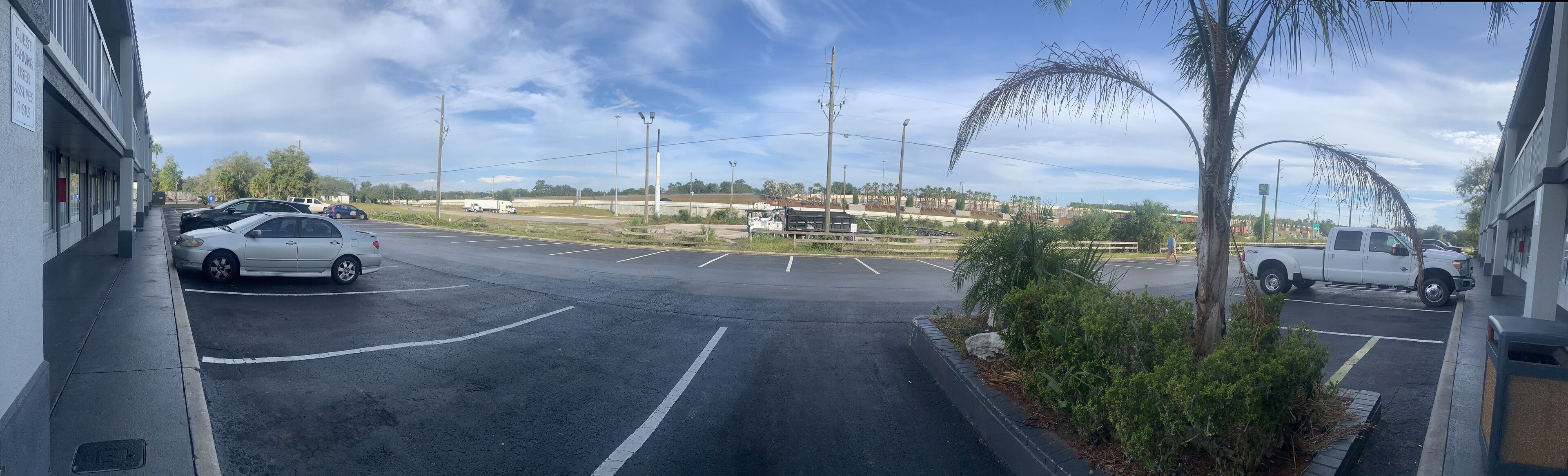 A parking lot with several cars and a truck, a pedestrian crossing, and a building with a sign indicating guest parking.
