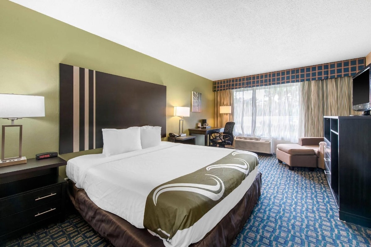 A hotel room with a large bed, a desk, a chair, a television, and a window with curtains.