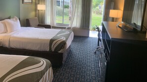 Una habitació d'hotel amb un llit gran, una taula amb televisió, una cadira i una finestra amb cortines.