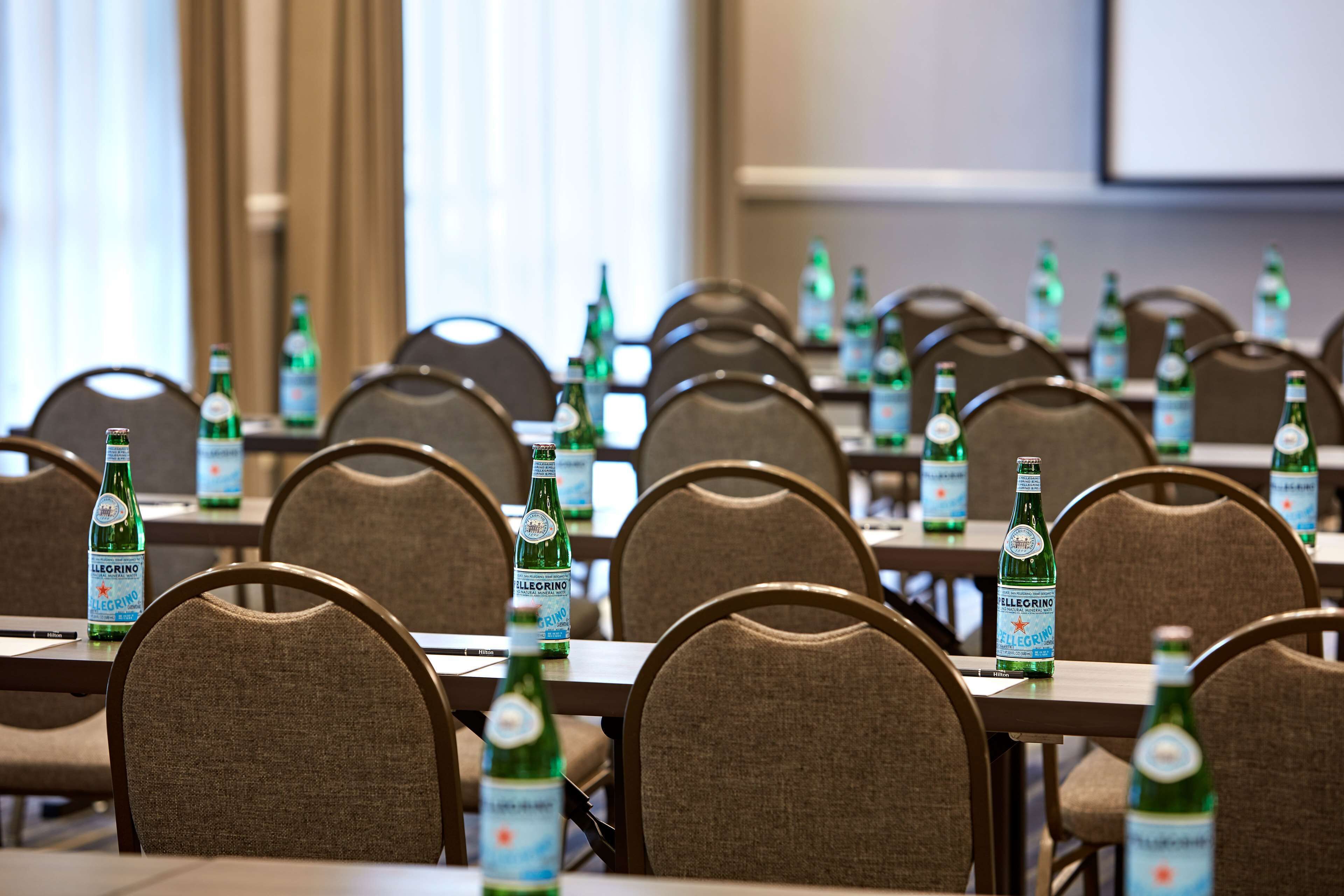 Een vergaderzaal met tafels klaar voor een vergadering, elk met een flesje Pellegrino water.