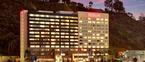 Un hotel de varios pisos con un llamativo letrero de 'Hilton', que presenta un diseño arquitectónico moderno con numerosas ventanas y un techo plano.