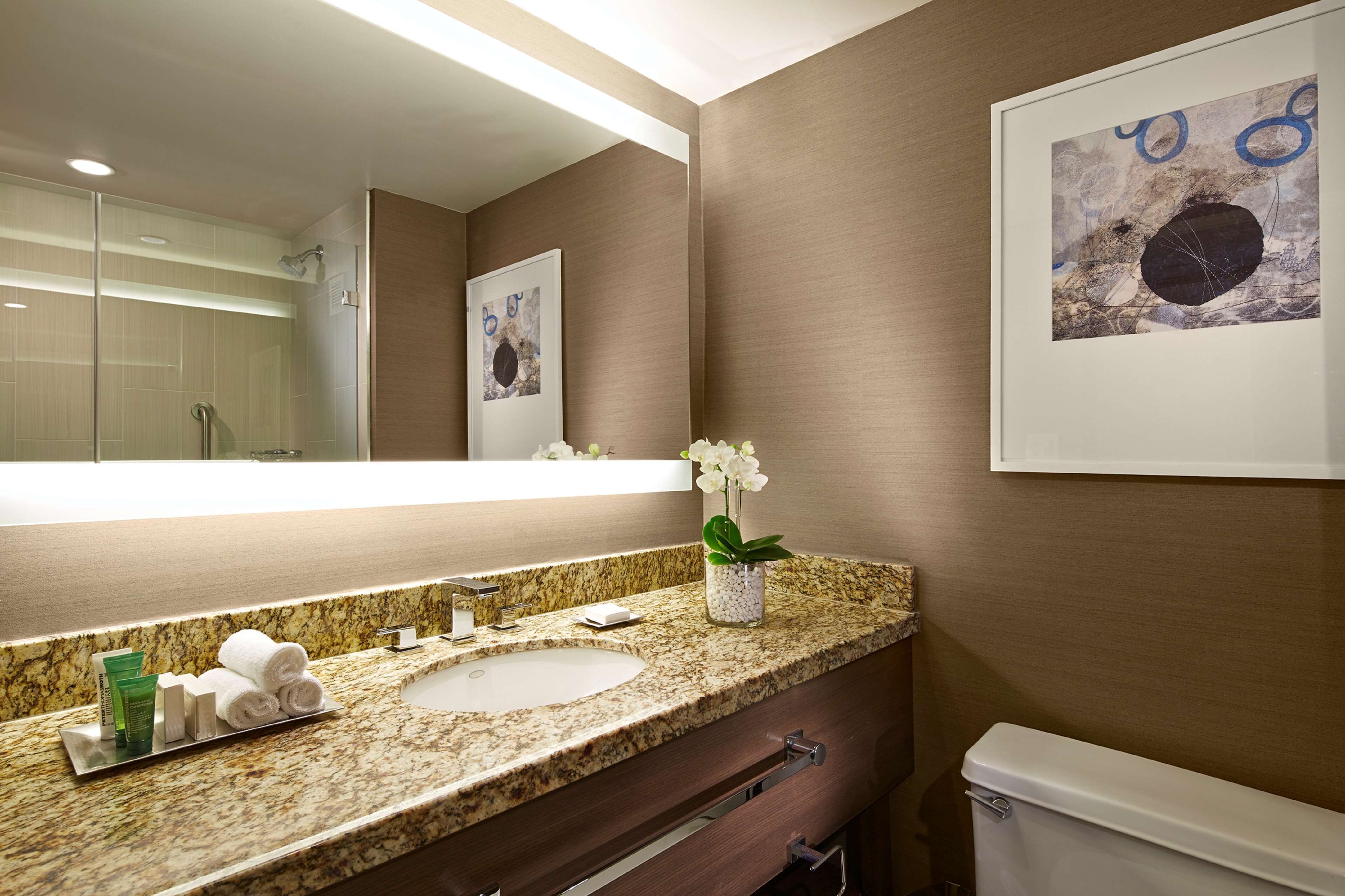 A bathroom with a marble sink, a glass shower enclosure, and a framed artwork on the wall.