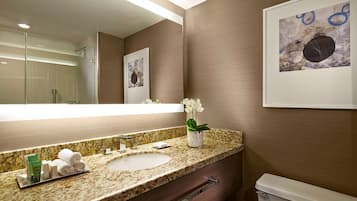 A bathroom with a marble sink, a glass shower enclosure, and a framed artwork on the wall.