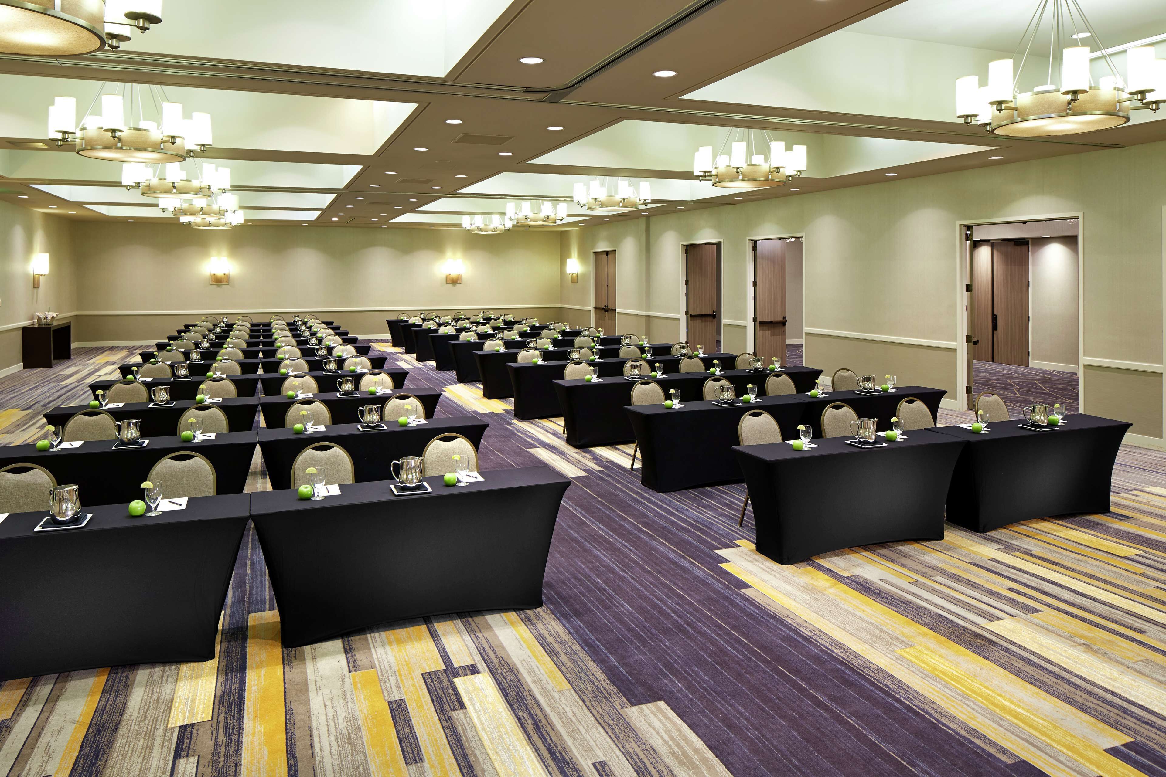 A conference room with rows of tables, chairs, and a carpeted floor.
