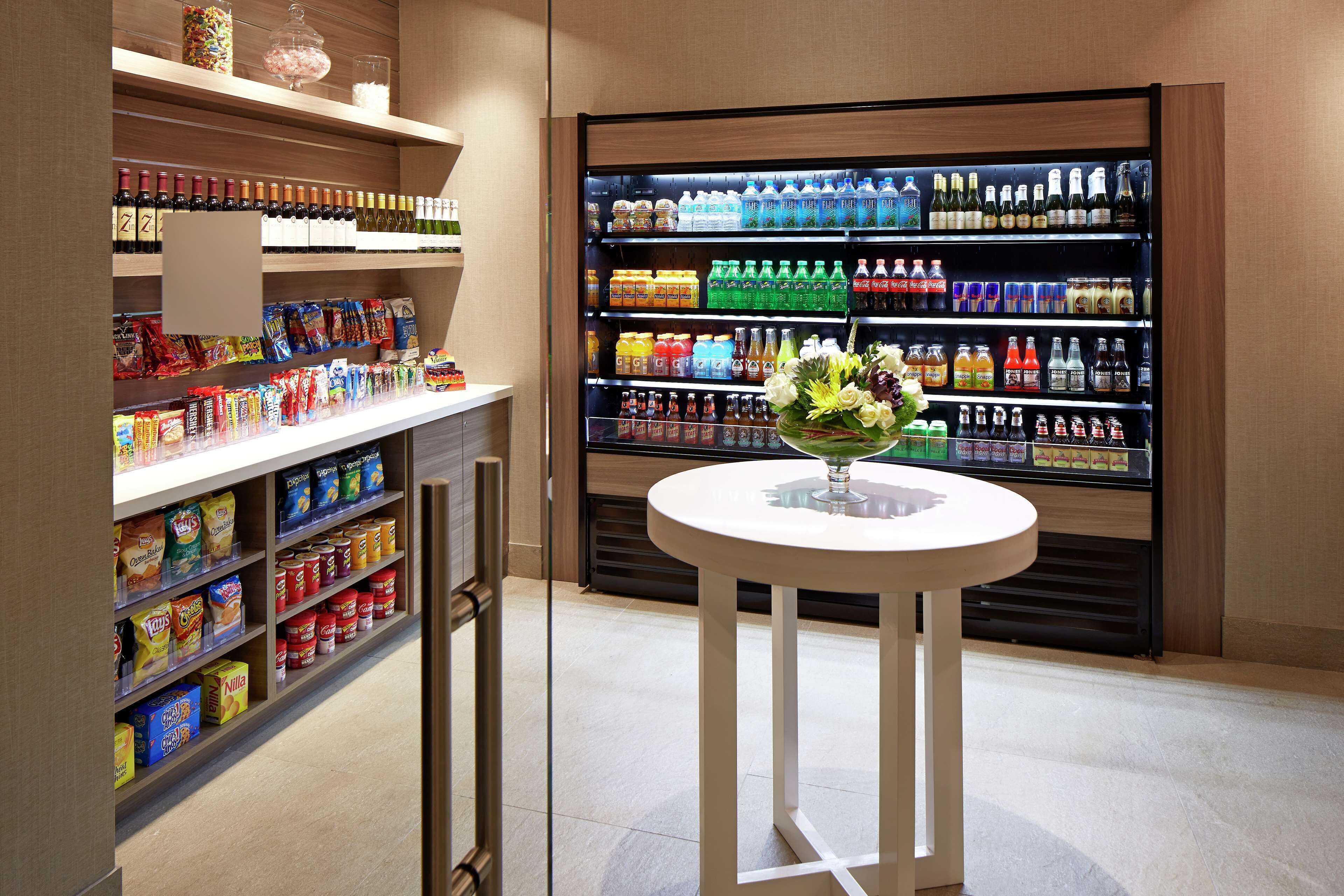 Een netjes ingerichte ruimte met drankjes en snacks, met een divers assortiment producten en een klein tafeltje met een bloevas.