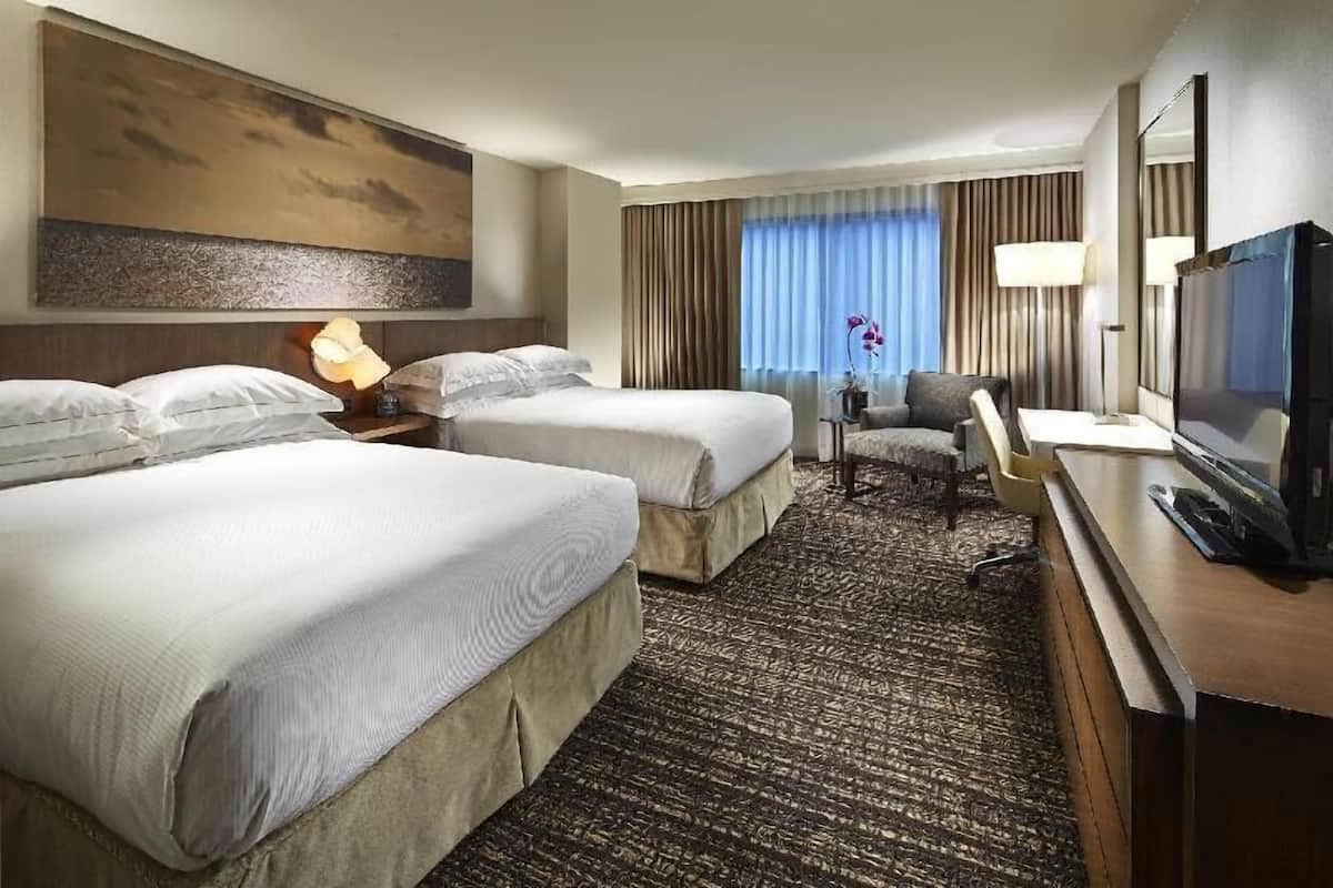A hotel room with two beds, a desk, a television, and a large painting on the wall.