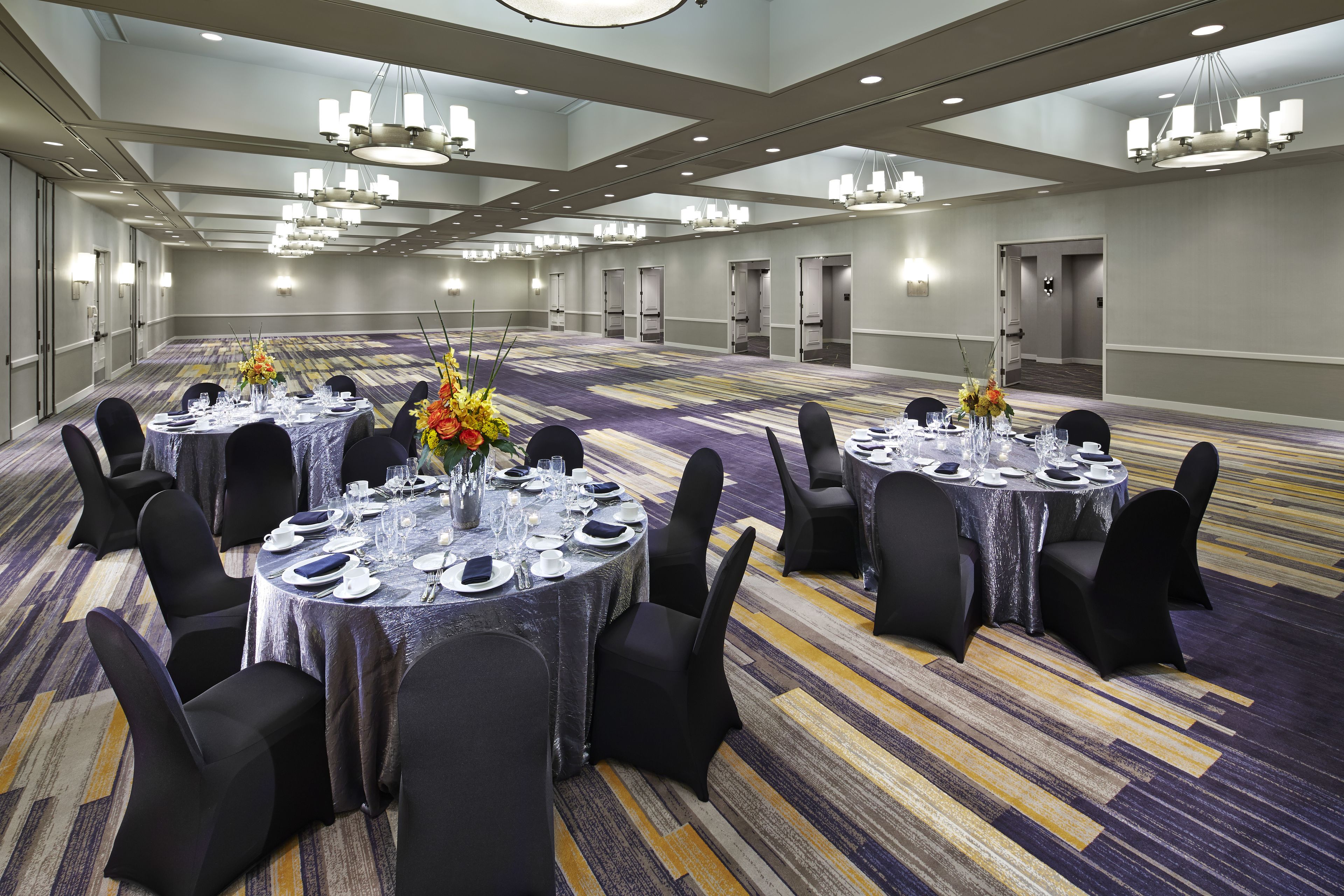 A large conference room with round tables set for dining, black chairs, and chandeliers.
