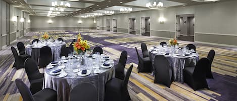 A large conference room with round tables set for dining, black chairs, and chandeliers.