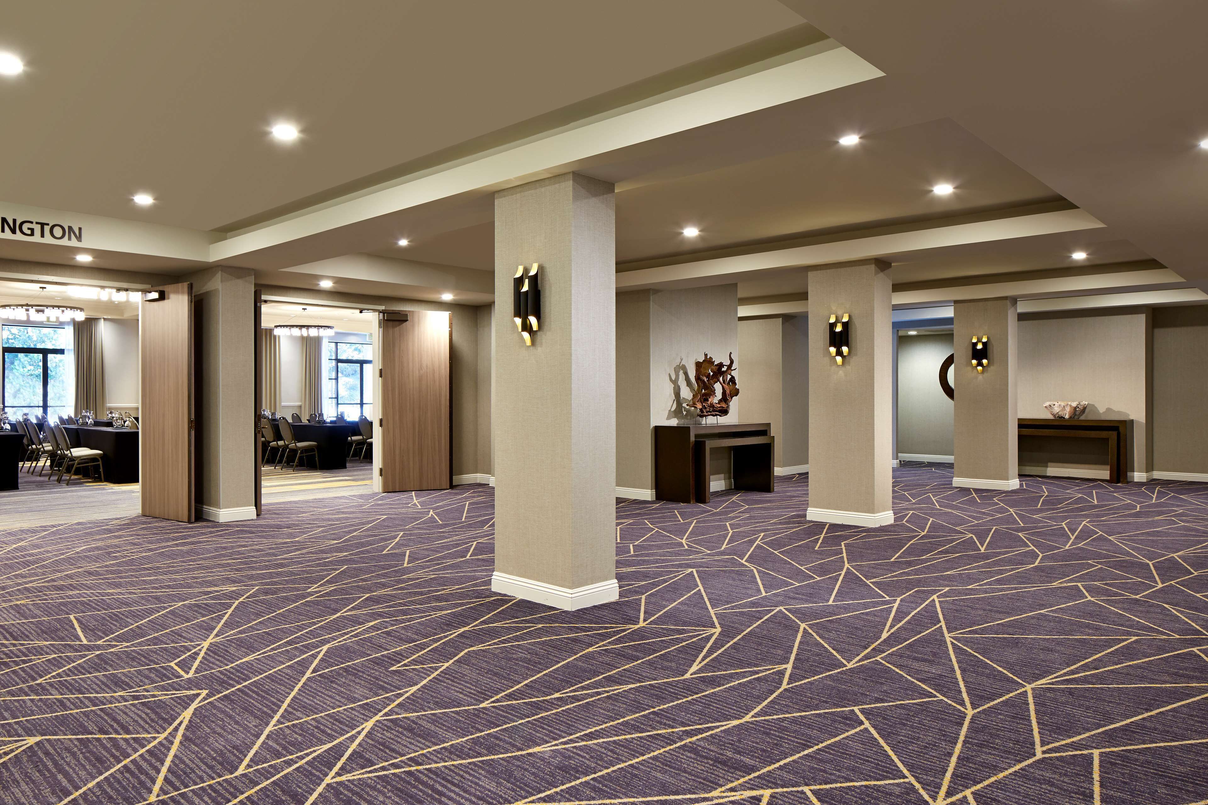 A spacious conference room with a patterned carpet, multiple columns, and a reception area with a sign reading "WASHINGTON".