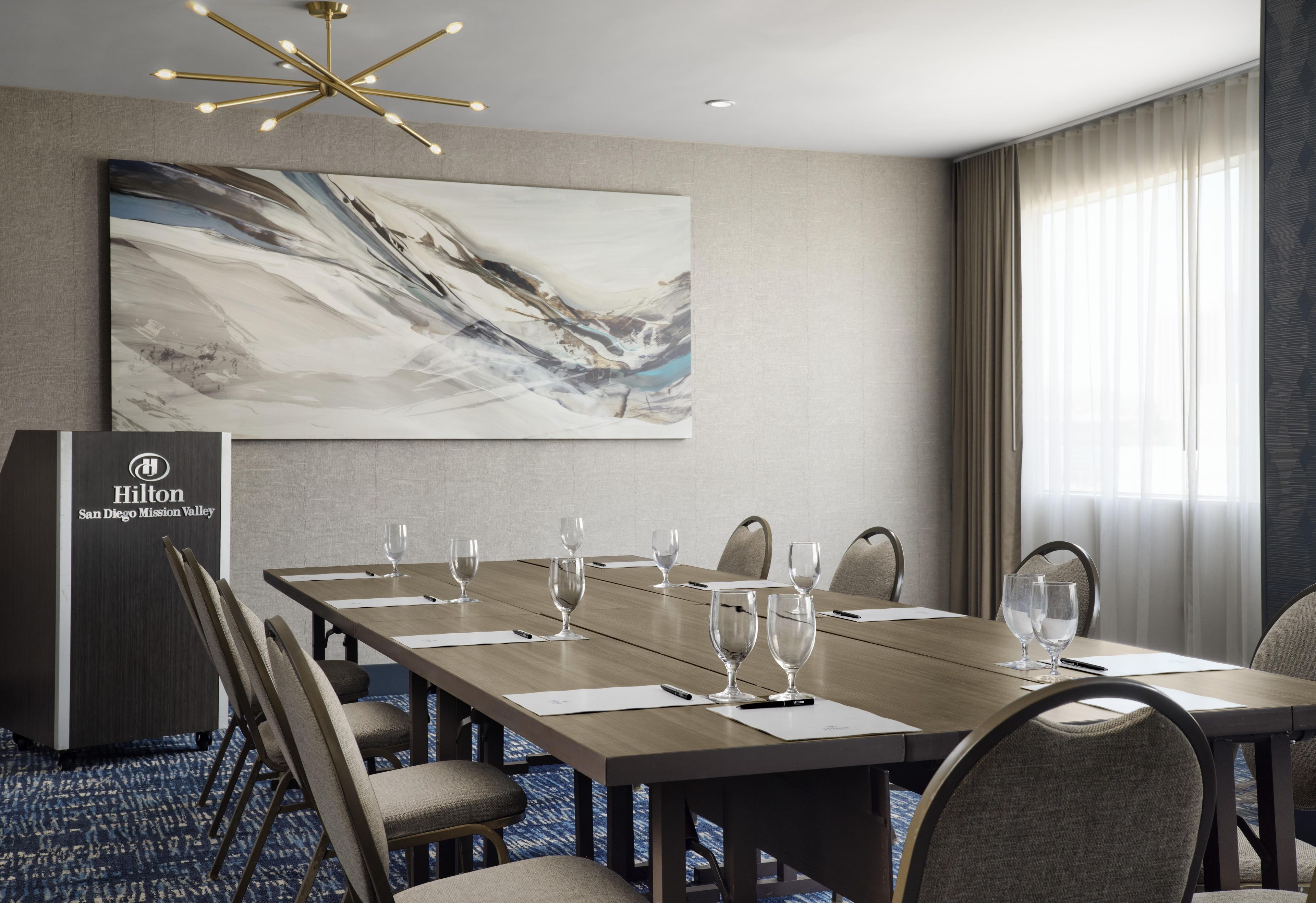 Une salle de conférence avec une longue table, des chaises et un grand tableau abstrait accroché au mur.