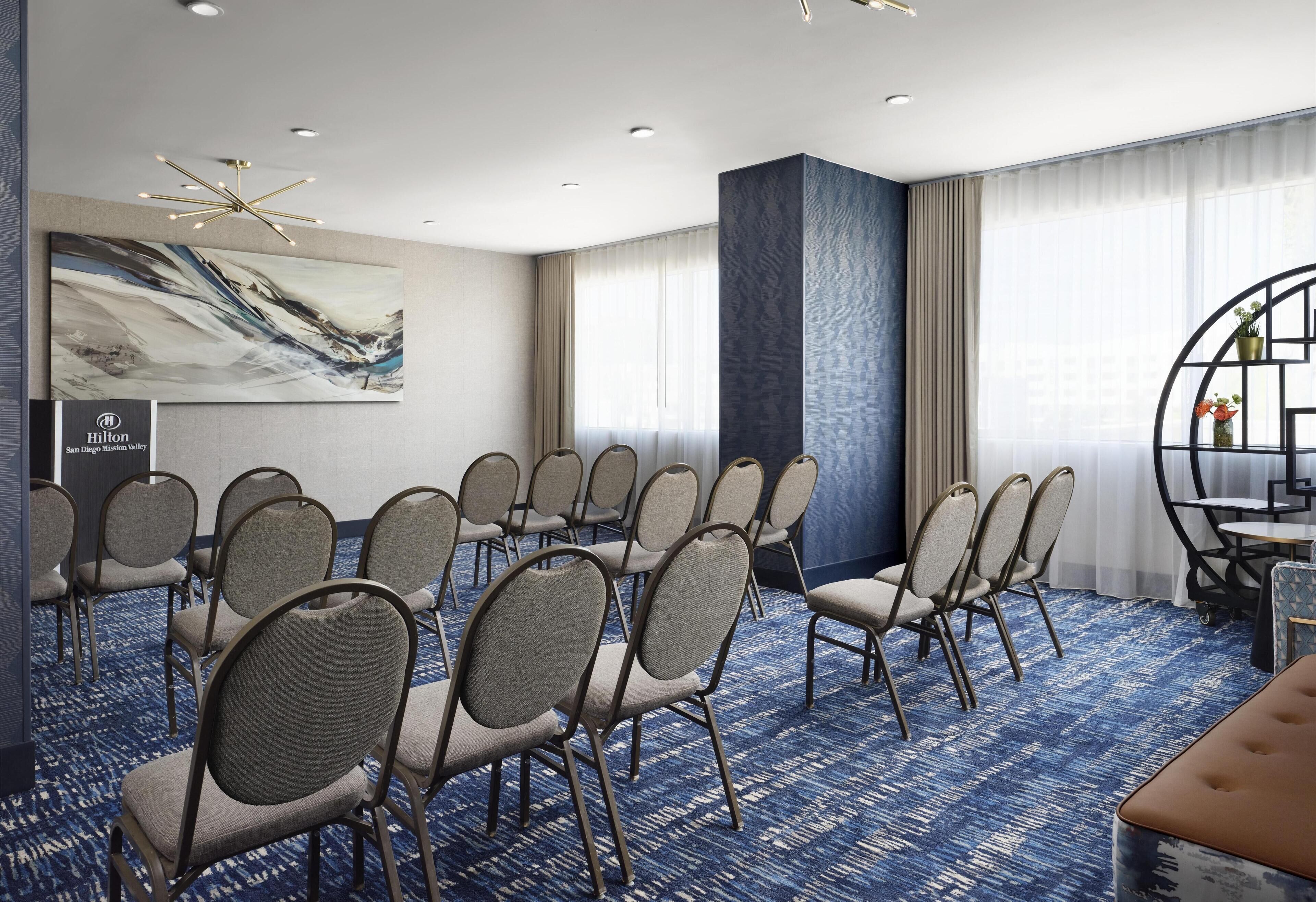 A conference room with rows of chairs, a large abstract painting, and a Hilton sign.