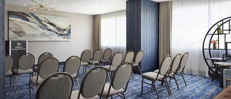 A conference room with rows of chairs, a large abstract painting, and a Hilton sign.