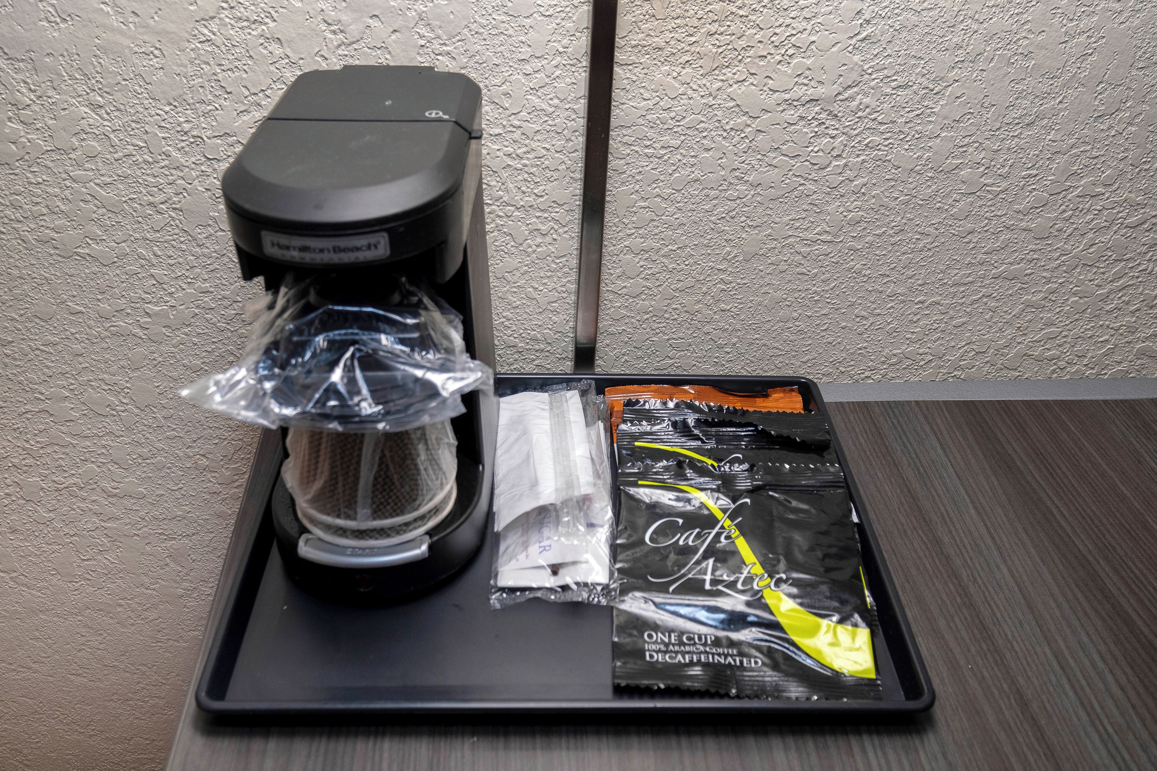 A coffee maker on a tray with a coffee bag labeled 'Cafe Art Deco Decaffeinated.'