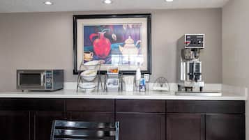 A kitchen with a commercial microwave oven, a coffee machine, and a framed painting above the counter.