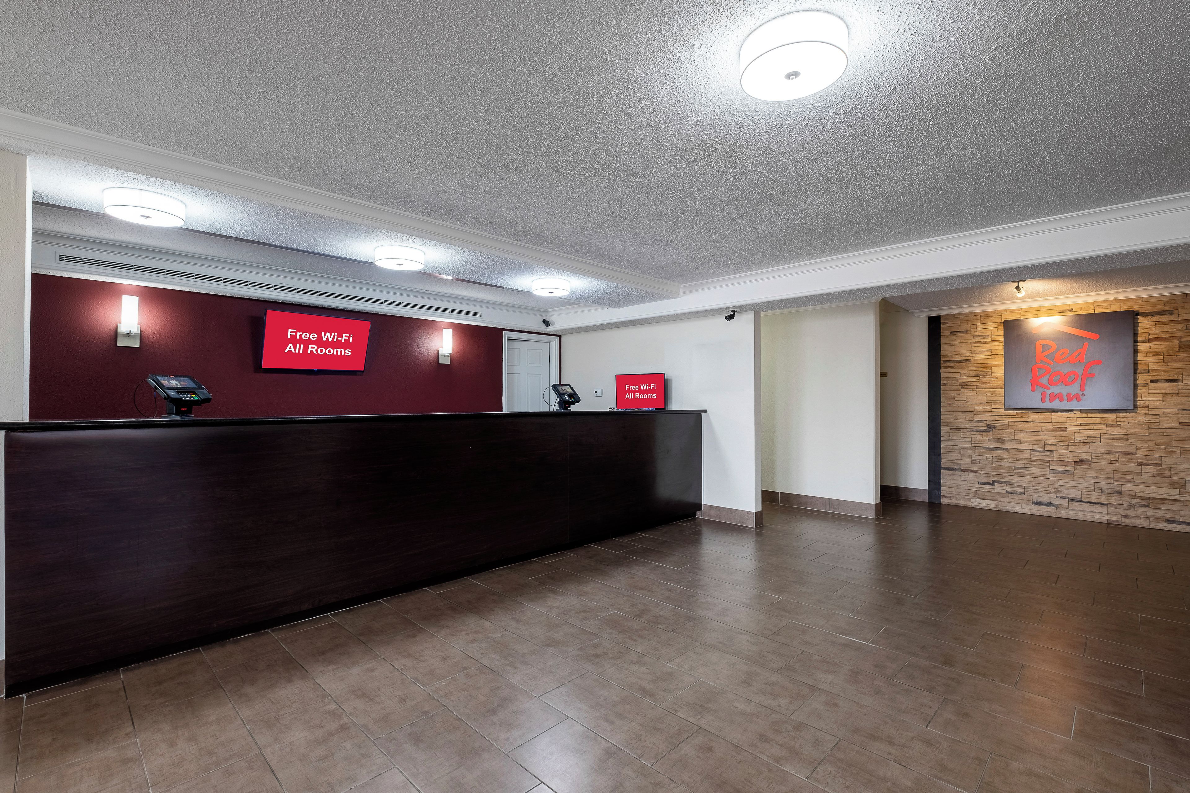 Ett receptionsområde med en mörk receptionsdisk, två skyltar som visar att det finns kostnadsfritt Wi-Fi i alla rum, och en skylt för Red Roof Inn på väggen.